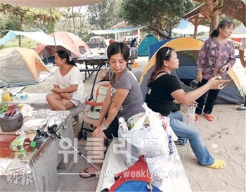 ▲ 홍콩시민 호타이(何太)가 캠프장에서 바비큐를 할 준비를 하는 사이 한 중국인 관광객이 비어 있는 옆자리를 차지하고 앉아 가져온 음식을 먹고 있다. 또 다른 중국인은 호타이의 등을 마주대고 앉아 휴식을 취하고 있다. <사진 출처 : 명보(明報) >