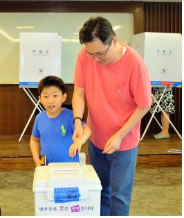 투표는 이렇게. 고사리 같은 아이의 손을 잡고 민주주의 꽃을 피우고 있는 자상한 아버지 유권자.